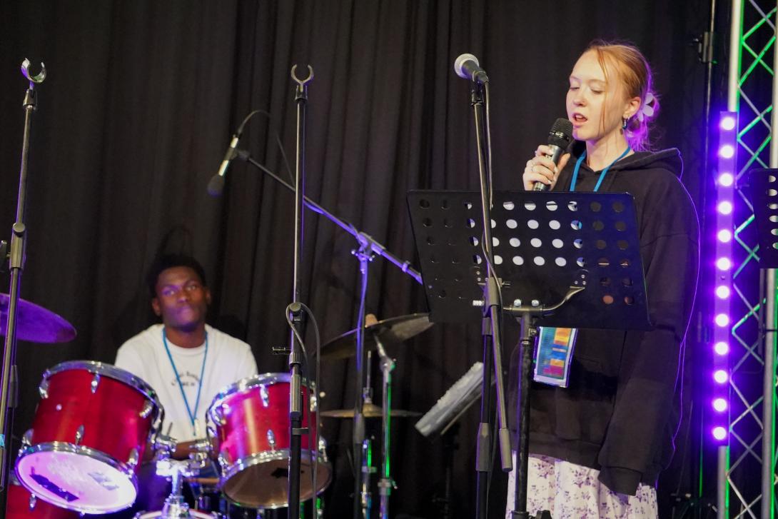 Woman worshipping on a stage with drummer in the background